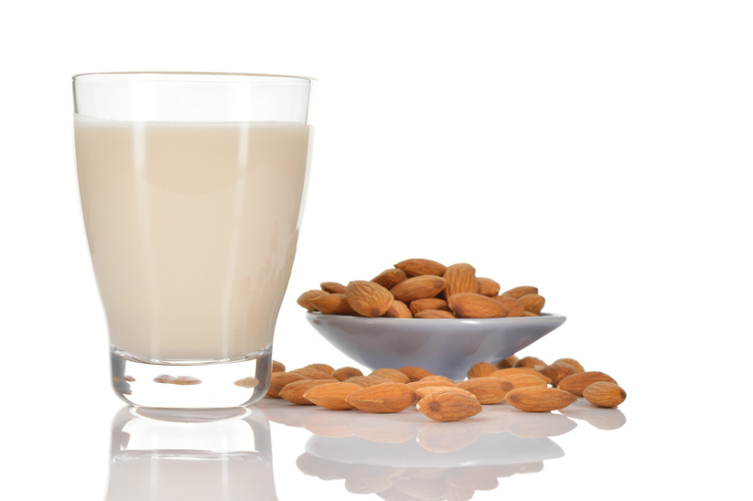 glass of almond milk with some almonds on the table
