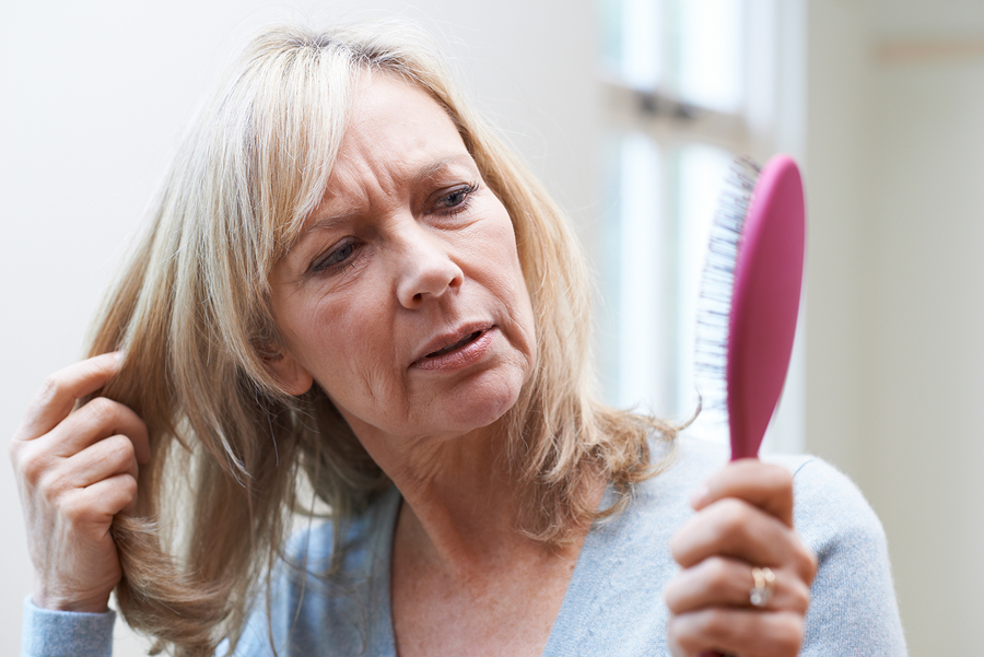 Woman holding her hair and a hairbrush looking concerned about hair loss