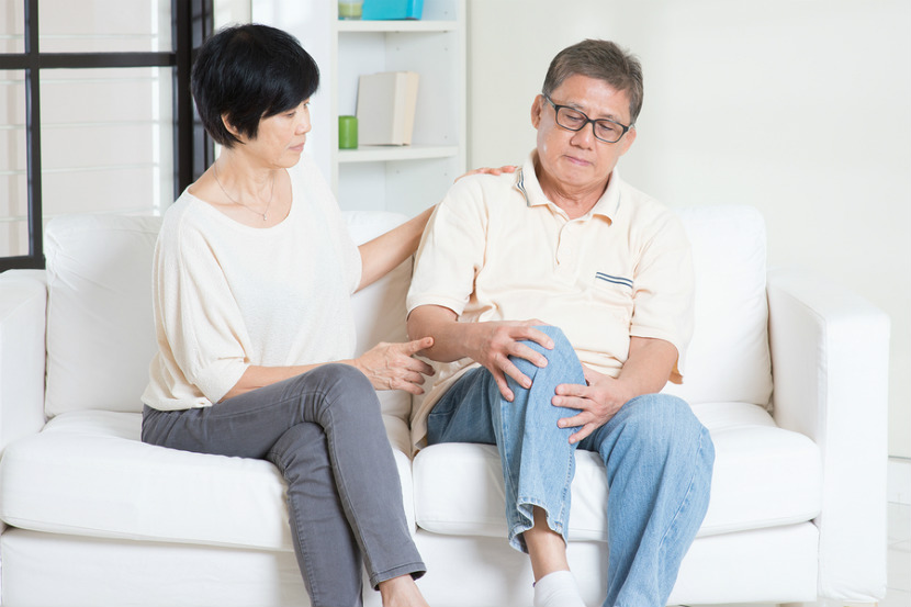 couple sitting on the couch with a man holding his knee in pain