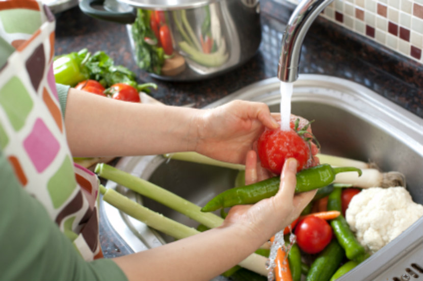 person washing vegetables and fruit under running water in kitchen