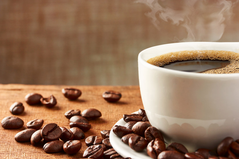 steaming cup of hot coffee surrounded by coffee beans