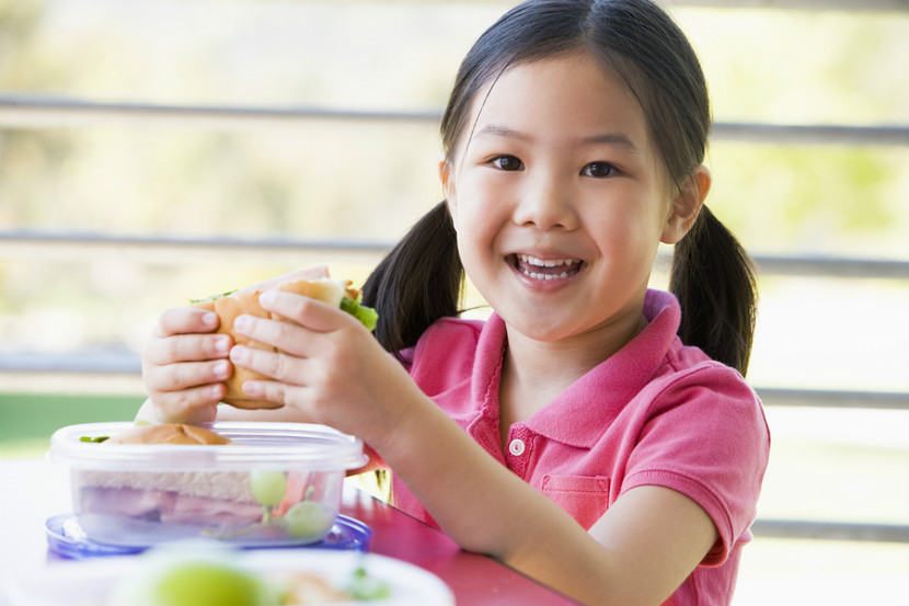 Une fille qui mange un sandwich et un fruit avec bonheur pendant le dîner à l’école