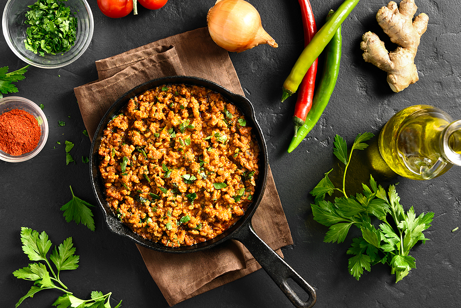 skillet filled with curry and surrounded by vegetables and spices