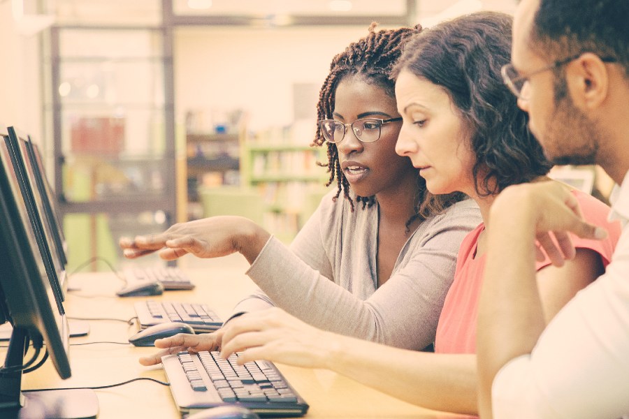 two women and a man working on a computer in an office