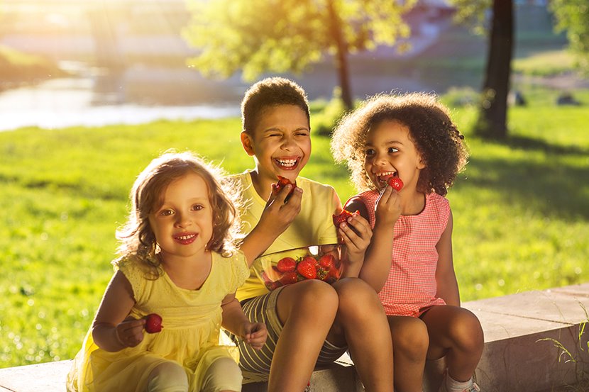 Three happy children eating strawberries on a sunny afternoon