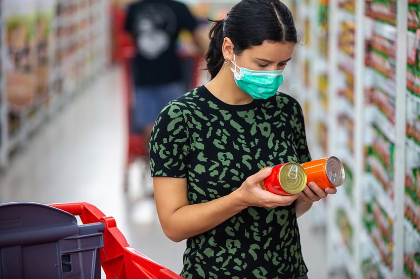Une femme portant un masque facial qui compare les étiquettes d’aliments à l’épicerie